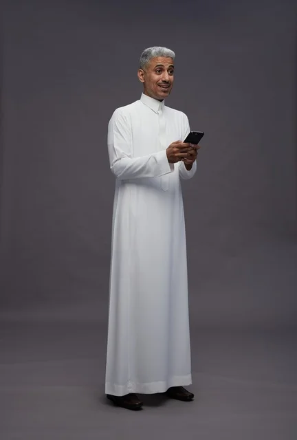رجل سعودي يستخدم هاتف ذكي بالثوب التقليدي في استوديو