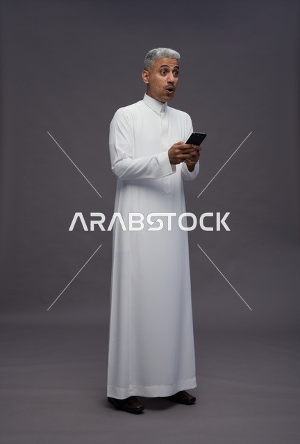 رجل سعودي بالزي التقليدي يستخدم هاتفاً ذكياً
