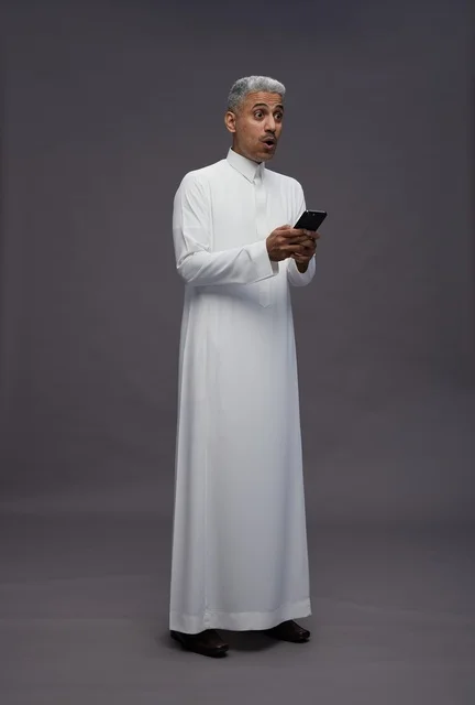 رجل سعودي بالزي التقليدي يستخدم هاتفاً ذكياً