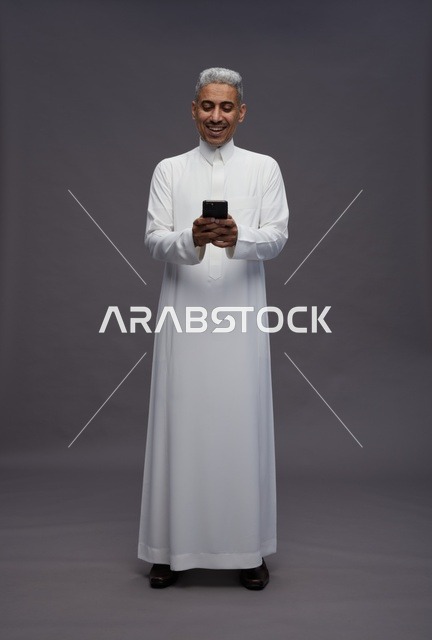 رجل سعودي بالزي التقليدي يستخدم هاتفاً ذكياً