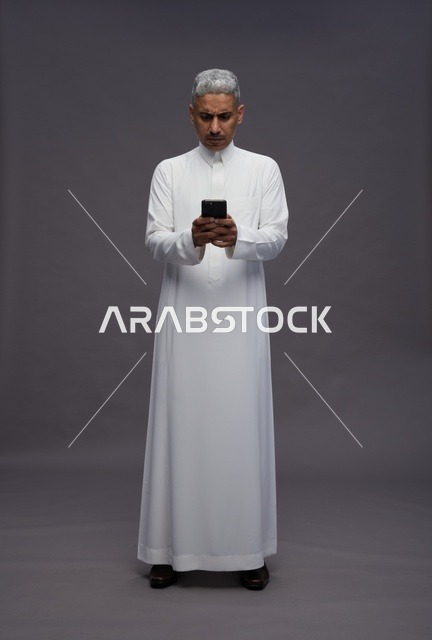 رجل سعودي بالثوب التقليدي يستخدم الهاتف في الاستوديو