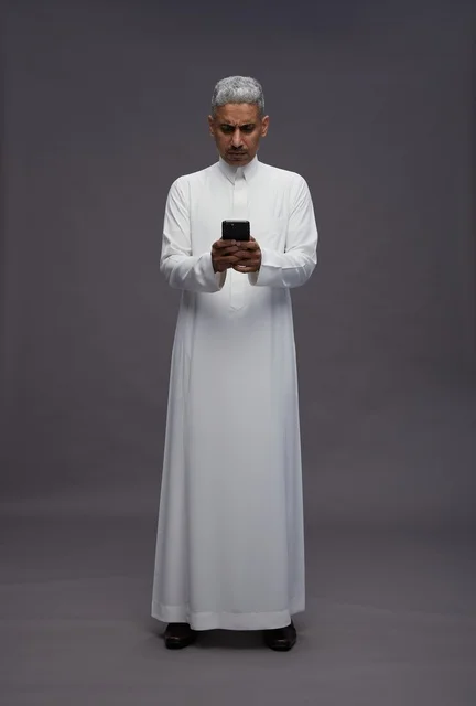 Saudi Man in Traditional Thobe Using Smartphone Studio