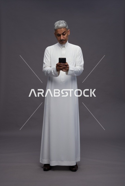 رجل سعودي بالثوب التقليدي يستخدم الهاتف الذكي