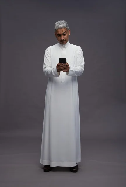 رجل سعودي بالثوب التقليدي يستخدم الهاتف الذكي