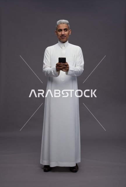 رجل سعودي بالزي التقليدي يستخدم الهاتف الذكي