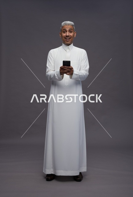 رجل سعودي بالزي التقليدي يستخدم هاتفاً ذكياً