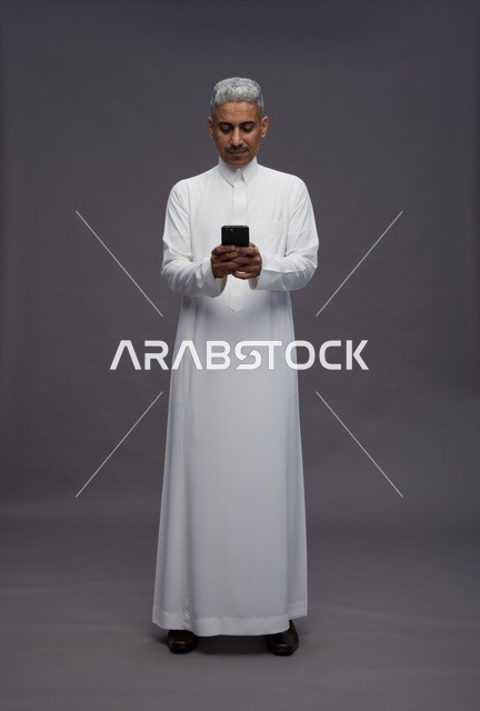 رجل سعودي بالثوب يستخدم الهاتف الذكي في الاستوديو