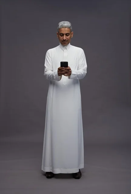 رجل سعودي بالثوب يستخدم الهاتف الذكي في الاستوديو