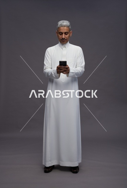رجل سعودي بالزي التقليدي يستخدم هاتفاً ذكياً