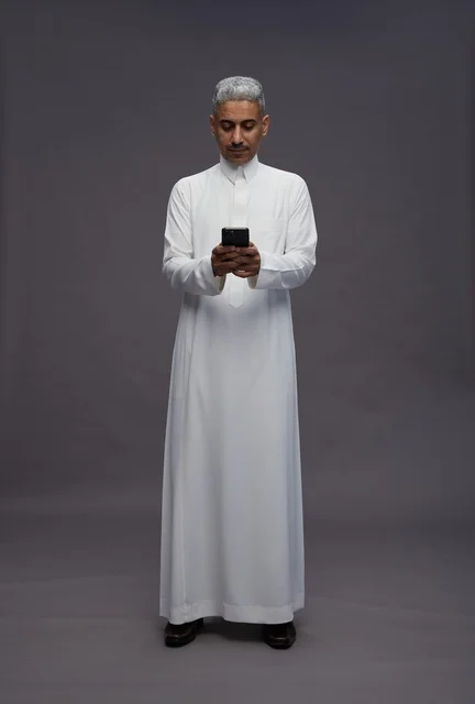 رجل سعودي بالزي التقليدي يستخدم هاتفاً ذكياً