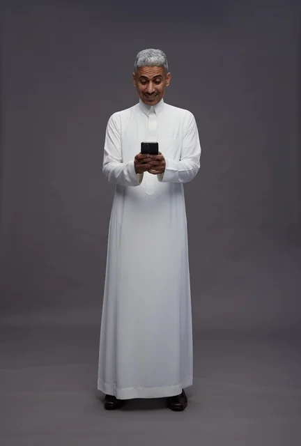 رجل سعودي بالزي التقليدي يستخدم الهاتف الذكي