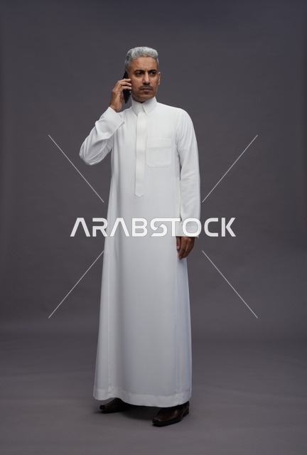رجل سعودي بالثوب الأبيض يتحدث عبر الهاتف الجوال