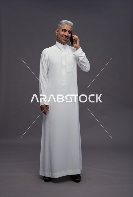 رجل سعودي بالثوب الأبيض يتحدث بالهاتف الذكي في الاستوديو