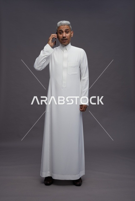 رجل سعودي بالثوب الأبيض يتحدث بالهاتف متفاجئ