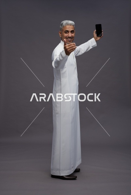 رجل سعودي بالثوب الأبيض يستخدم الجوال في الاستوديو