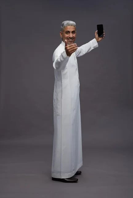 رجل سعودي بالثوب الأبيض يستخدم الجوال في الاستوديو