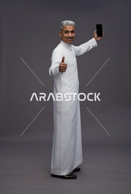 رجل سعودي بالثوب يحمل هاتف ذكي مع إشارة موافقة