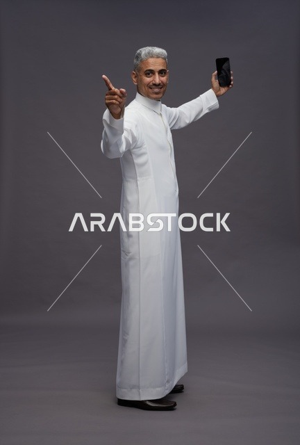 رجل سعودي بالثوب الأبيض يحمل هاتف ذكي في استوديو