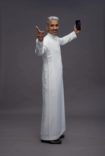 Saudi Man in White Thobe Holding Smartphone in Studio