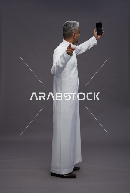 رجل سعودي بالثوب التقليدي يلتقط صورة سيلفي بالهاتف