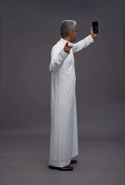 رجل سعودي بالثوب التقليدي يلتقط صورة سيلفي بالهاتف