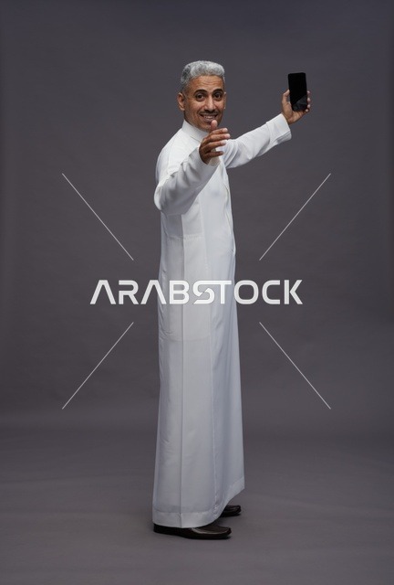 رجل سعودي بالثوب التقليدي يلتقط سيلفي بالهاتف