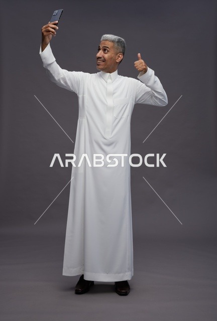 Saudi Man in Thobe Taking Selfie in Studio Thumbs Up