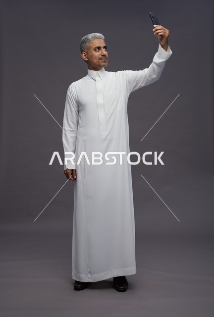 رجل سعودي بالثوب الأبيض يلتقط صورة سيلفي بالجوال