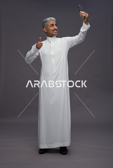 رجل سعودي بالثوب التقليدي يلتقط سيلفي بالهاتف الذكي