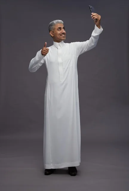 رجل سعودي بالثوب التقليدي يلتقط سيلفي بالهاتف الذكي