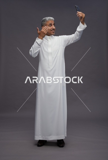 رجل سعودي بالثوب التقليدي يلتقط سيلفي في الاستوديو