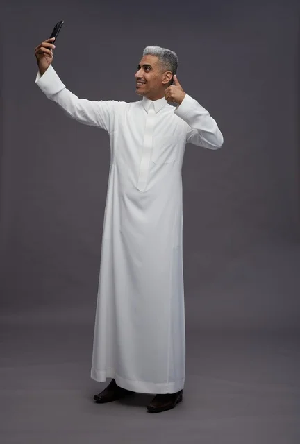 رجل سعودي بالثوب يلتقط صورة سيلفي على خلفية رمادية