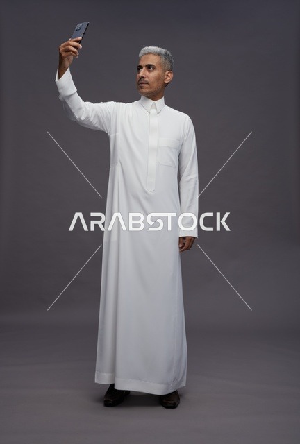 رجل سعودي بالثوب التقليدي يلتقط سيلفي في الاستوديو