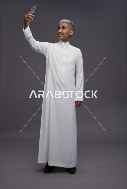 رجل سعودي بالثوب التقليدي يلتقط صورة سيلفي بالجوال