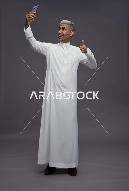 رجل سعودي بالثوب التقليدي يلتقط سيلفي بعلامة الإعجاب