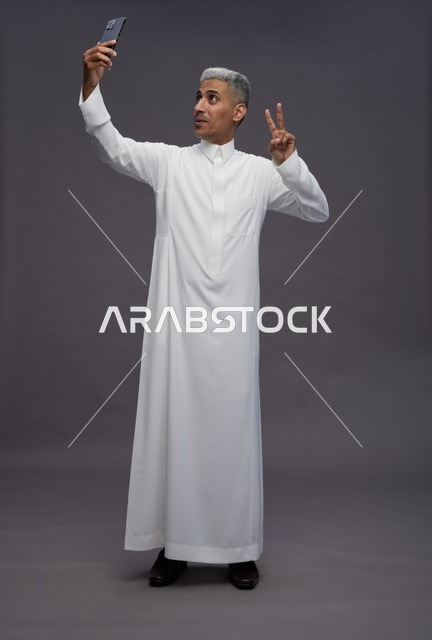 رجل سعودي بالثوب يلتقط سيلفي في الاستوديو