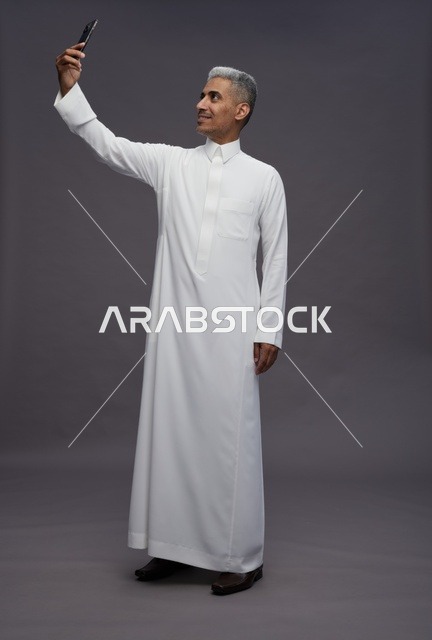 رجل سعودي بالثوب الأبيض التقليدي يلتقط صورة سيلفي