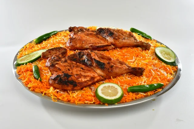 A plate of Saudi red mandi rice with roasted chicken, popular orange-colored rice, traditional Saudi popular restaurant, white background.