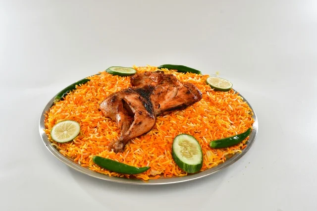 طبق من الرز المندي الاحمر السعودي مع الدجاج المحمر , أرز شعبي باللون البرتقالي , مطعم سعودي شعبي تقليدي, خلفيه بيضاء