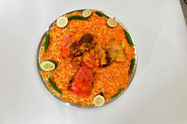 طبق من الرز المندي الاحمر السعودي مع الدجاج المحمر , أرز شعبي باللون البرتقالي , مطعم سعودي شعبي تقليدي, خلفيه بيضاء