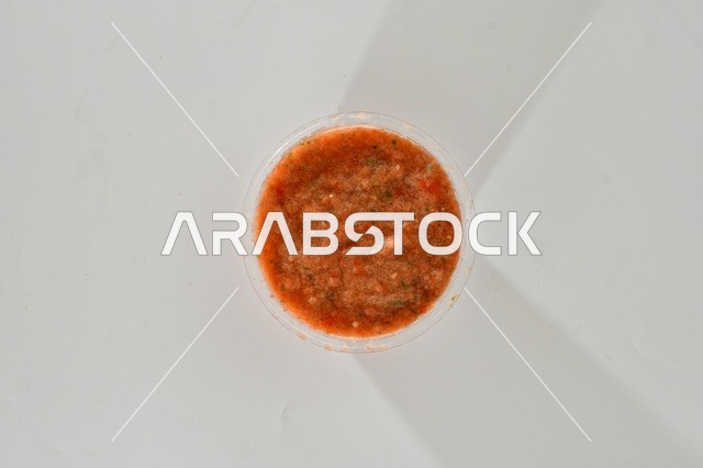 A vertical upper image of hot tomato sauce, traditional Saudi sauce, red salad with red pepper, popular Saudi appetizers, white background.
