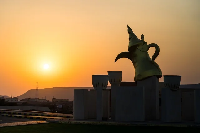 The view of the sunset at the Arabic coffee roundabout with coffee cups in the village of Mudrikah on the road to Jeddah in Mecca, a historic popular area, with mountainous terrain and paved roads in the city, Kingdom of Saudi Arabia.
