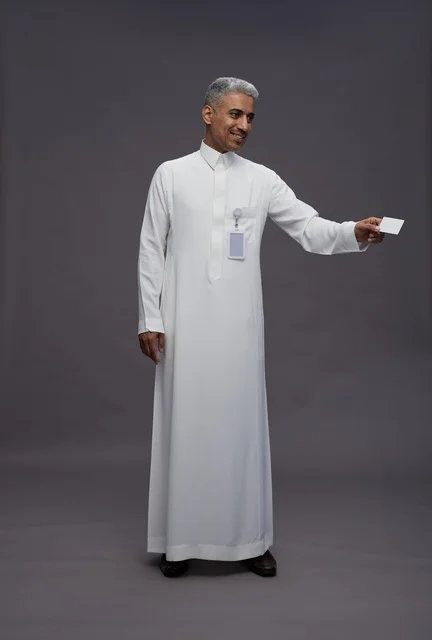 بورتريه لرجل عربي سعودي خليجي يرتدي الثوب الابيض يعرض بطاقة ائتمان بيضاء فارغه ويشير اليها, كرت تعريفي شخصي, الجسم بالكامل, خلفيه رماديه