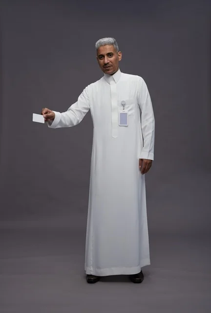 بورتريه لرجل عربي سعودي خليجي يرتدي الثوب الابيض يعرض بطاقة ائتمان بيضاء فارغه ويشير اليها, كرت تعريفي شخصي, الجسم بالكامل, خلفيه رماديه