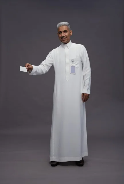 بورتريه لرجل عربي سعودي خليجي يرتدي الثوب الابيض يعرض بطاقة ائتمان بيضاء فارغه ويشير اليها, كرت تعريفي شخصي, الجسم بالكامل, خلفيه رماديه