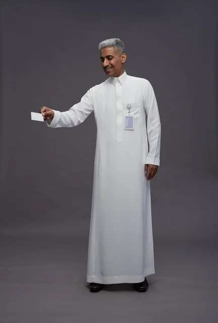 بورتريه لرجل عربي سعودي خليجي يرتدي الثوب الابيض يعرض بطاقة ائتمان بيضاء فارغه ويشير اليها, كرت تعريفي شخصي, الجسم بالكامل, خلفيه رماديه