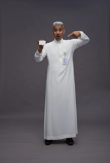 بورتريه لرجل عربي سعودي خليجي يرتدي الثوب الابيض يعرض بطاقة ائتمان بيضاء فارغه ويشير اليها, كرت تعريفي شخصي, الجسم بالكامل, خلفيه رماديه