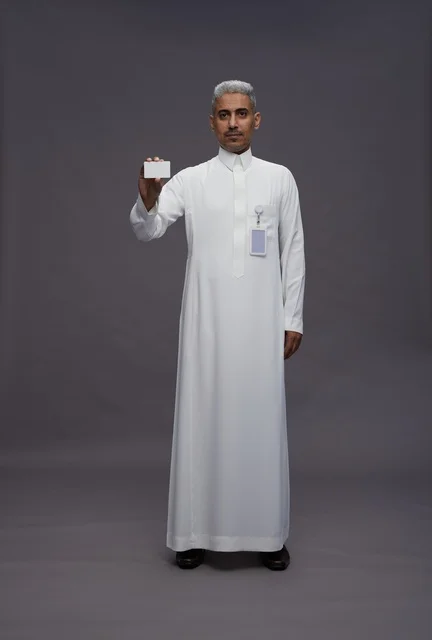 بورتريه لرجل عربي سعودي خليجي يرتدي الثوب الابيض يعرض بطاقة ائتمان بيضاء فارغه ويشير اليها, كرت تعريفي شخصي, الجسم بالكامل, خلفيه رماديه
