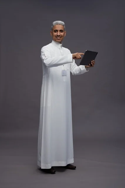 A portrait of an Arab Saudi Gulf man wearing a white thobe holding a mobile tablet in his hand, with various gestures and expressions, full body, gray background.