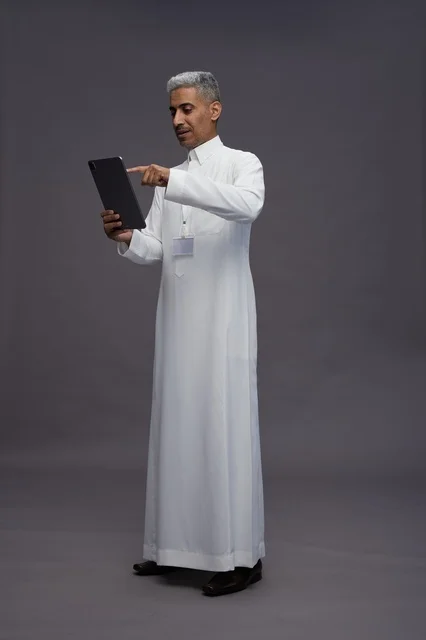 A portrait of an Arab Saudi Gulf man wearing a white thobe holding a mobile tablet in his hand, with various gestures and expressions, full body, gray background.